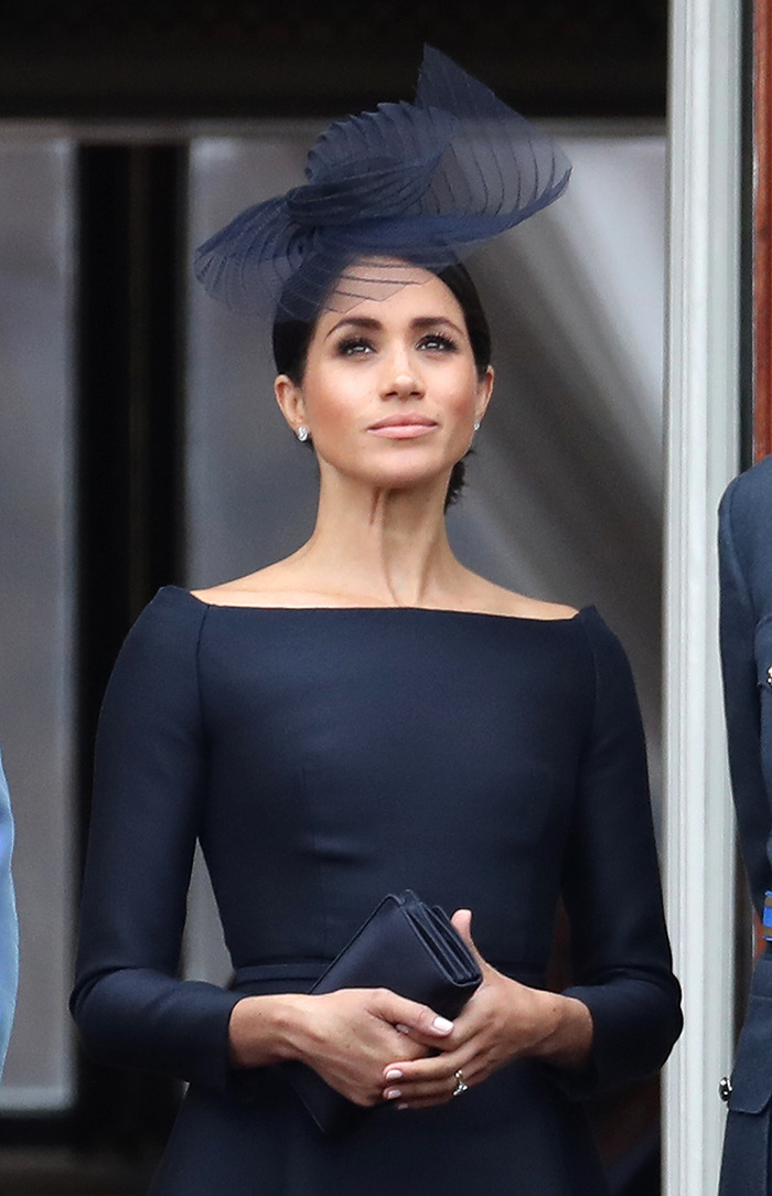 Meghan Markle in a neutral expression wearing navy outfit with hat.