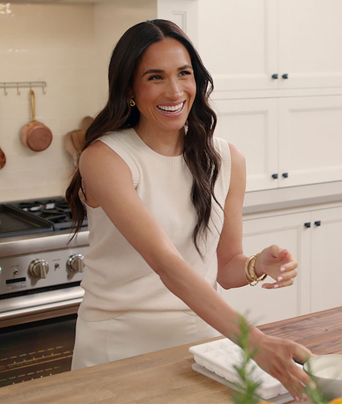 Woman in a kitchen smiling, wearing a sleeveless top, with hair down.