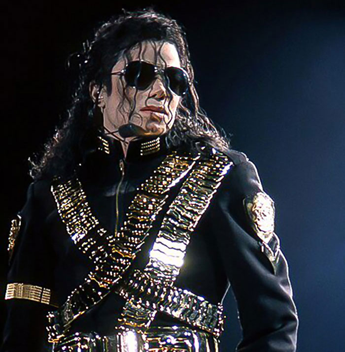 A performer in a dazzling black and gold outfit on stage, wearing sunglasses.