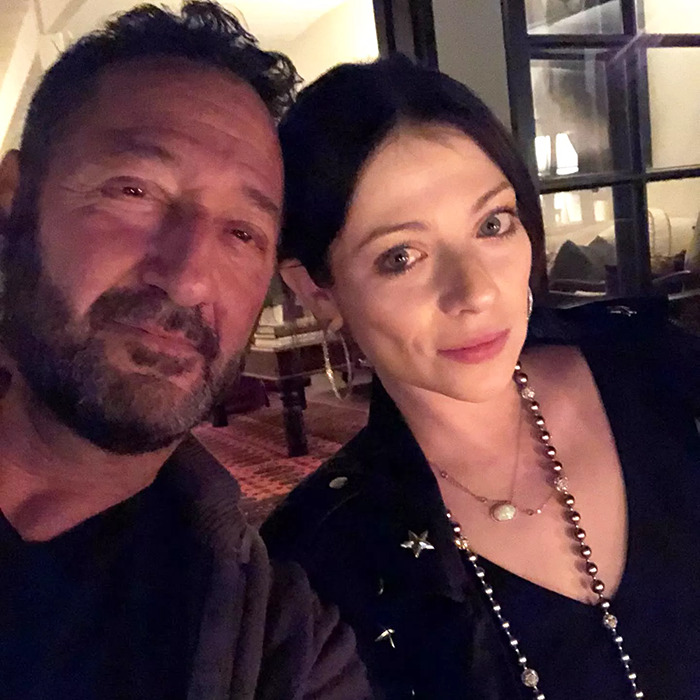 A woman and a man taking a selfie indoors, the woman wearing a necklace and earrings.