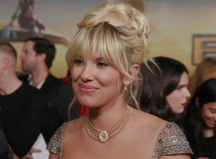 Millie Bobby Brown with blonde hair in an elegant dress at a premiere event, posing on the red carpet.