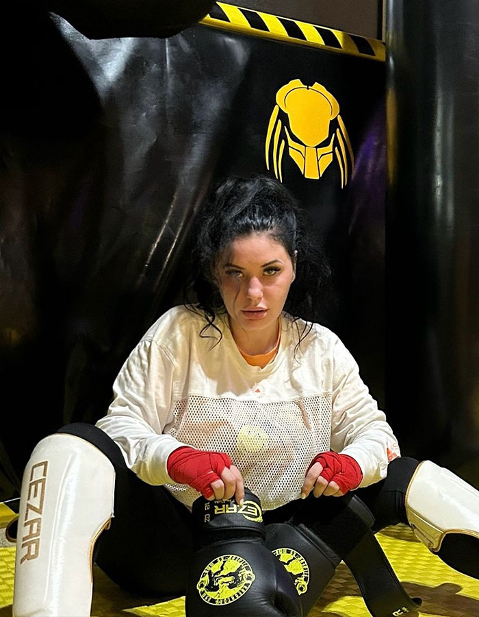 Woman in MMA gear, red gloves, preparing for controversial fight in gym setting.