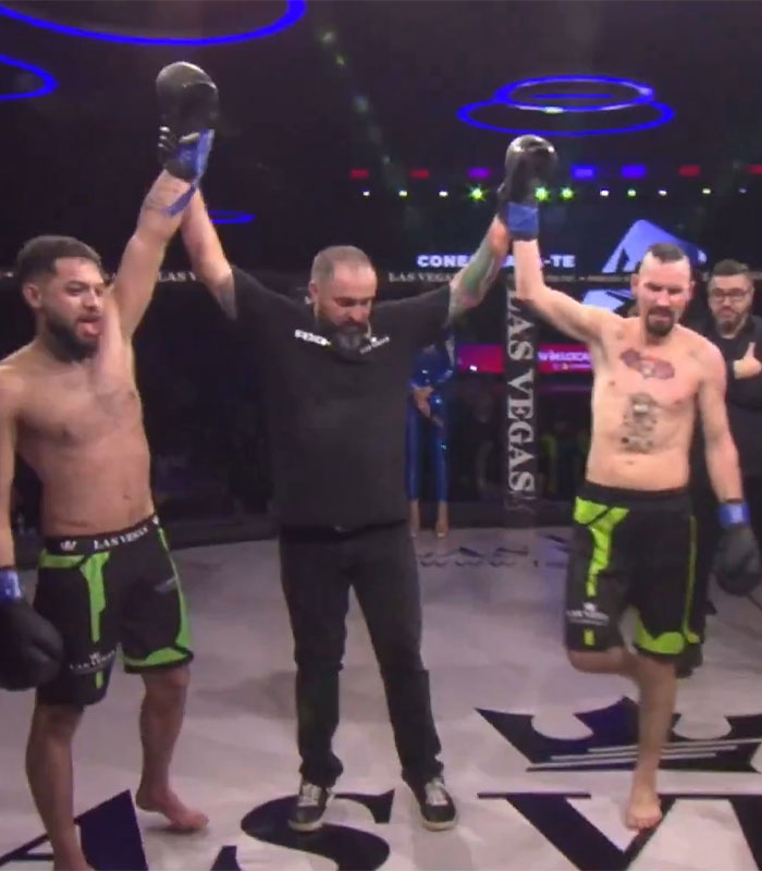 Two pro MMA fighters celebrating victory in a controversial fight, with a referee raising their hands.