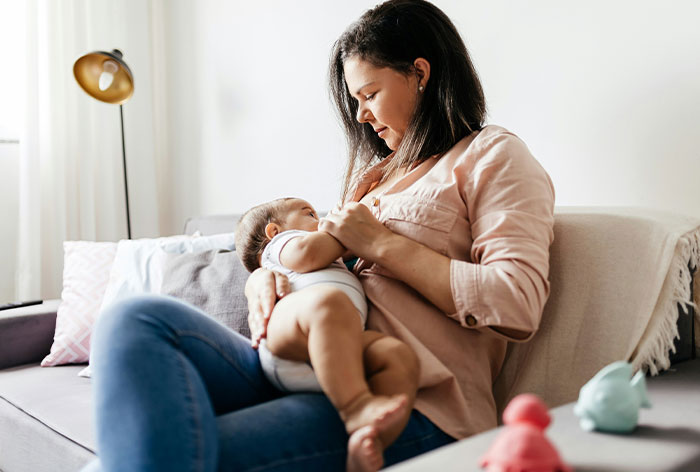 Mom holding baby on sofa, showing concern over 14YO helping responsibilities.