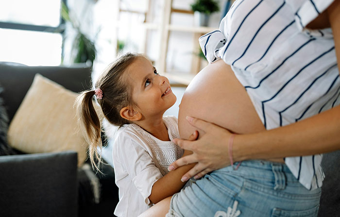 Child lovingly gazing at pregnant mom at home, highlighting growing up in family dynamics.