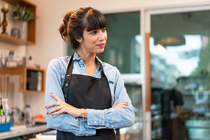 Worker in a denim shirt and apron stands with arms crossed, conveying a thoughtful expression.