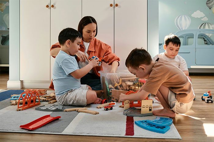 Mom with nine kids plays on the floor, surrounded by toys, capturing a moment of parenting and childcare activities.