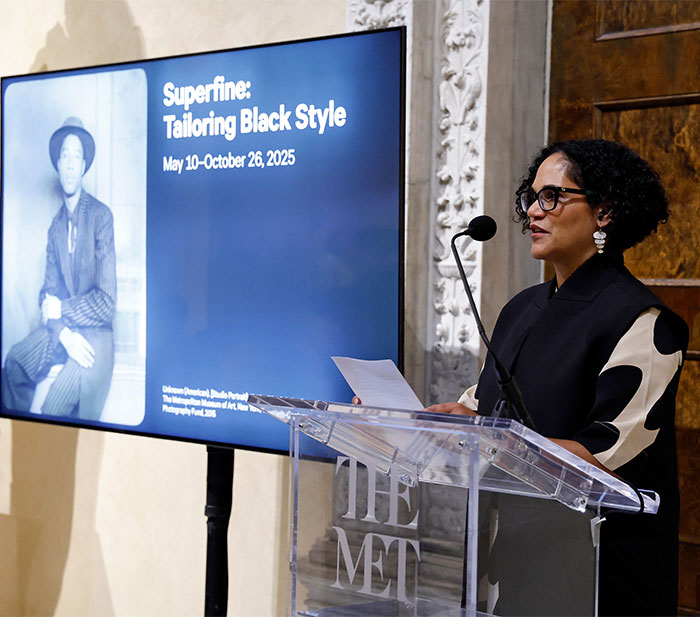 A woman speaks at a Met event, highlighting the 2025 dress code and the "Superfine: Tailoring Black Style" exhibit.