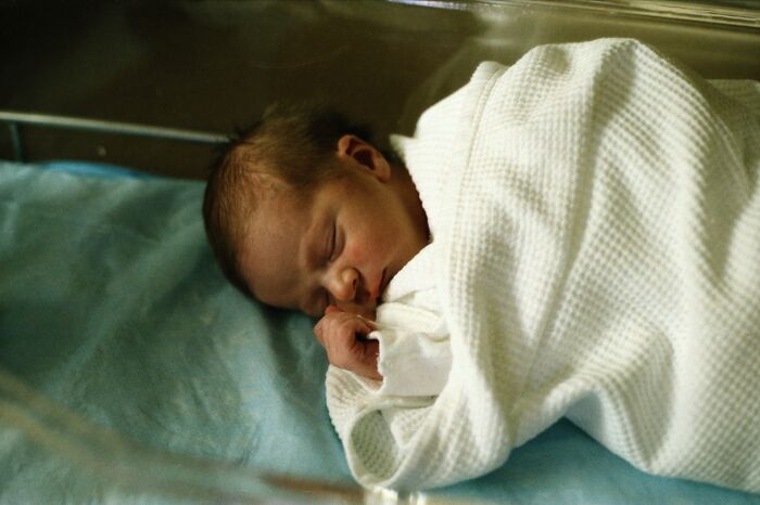 Newborn baby wrapped in a white blanket, peacefully sleeping in a hospital crib.