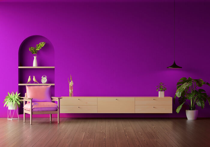 Lounge redecorated with purple walls, a pink chair, and plants; showcasing a modern interior design style.