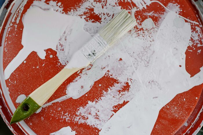 Paintbrush on a red paint can lid, illustrating redecorating efforts gone awry.