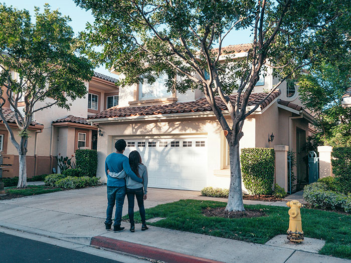 Couple standing in front of garage, contemplating neighbor parking car unauthorized in driveway.