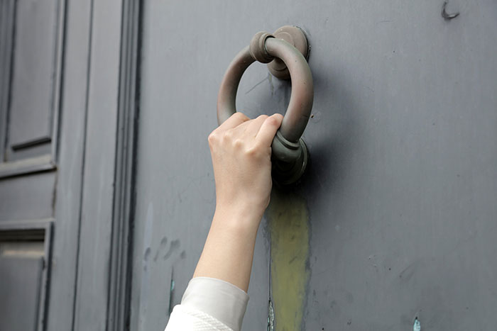 Hand knocking on a door, addressing issues with neighbor parking car unauthorized.