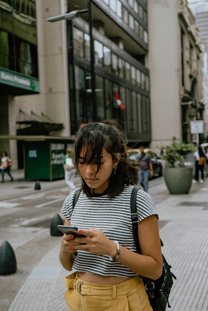 Gen Z individual on a city street using a smartphone, possibly sharing opinions on boomer complaints.