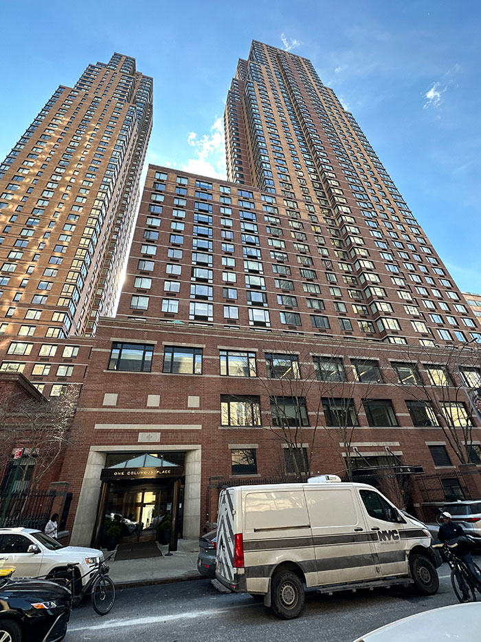 Urban landscape with high-rise buildings under a blue sky, featuring NYC vehicles on the street.