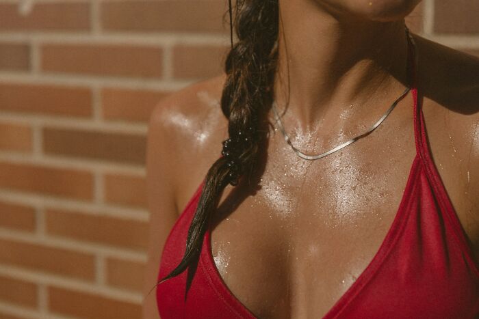 Close-up of a woman's torso wearing a red top in sunlight, highlighting the female body.