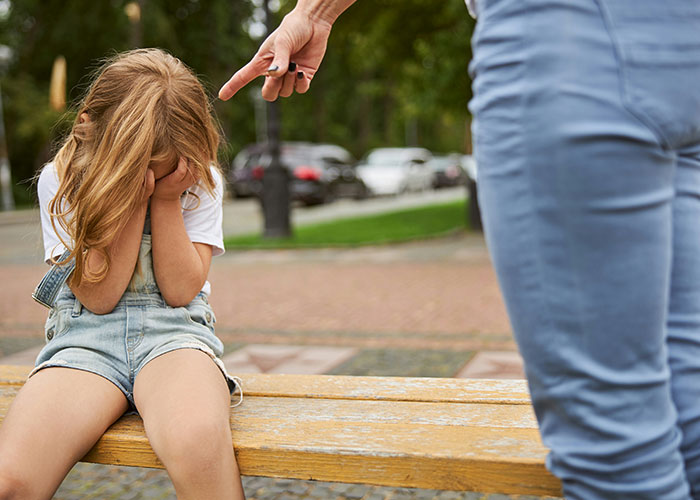 Parenting coach advises against yelling; upset child on bench while adult points a finger.