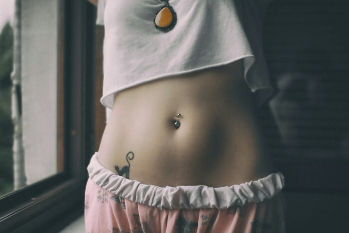 "Close-up of a woman's belly with a piercing and tattoo, highlighting unique aspects of the female body."