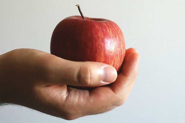 A hand holding a red apple against a plain background, capturing a mic-drop-moment in simplicity and everyday beauty.