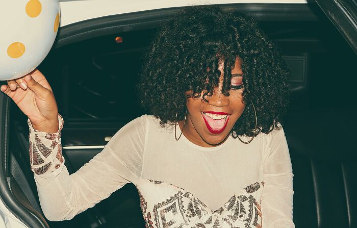 A childfree person joyfully exiting a car, smiling while holding a balloon, wearing a stylish patterned dress.