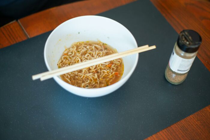 Bowl of instant noodles with chopsticks, on a table beside seasoning, illustrating travel must-haves for easy meals.