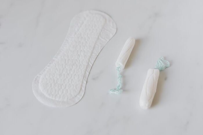 Feminine hygiene products on a marble surface, featuring a pad and two tampons with turquoise strings.