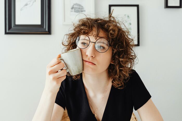 A person with curly hair and glasses holding a cup, contemplating life without kids.