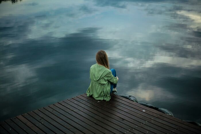 Person sitting on dock by a calm lake, reflecting on childfree life choices.