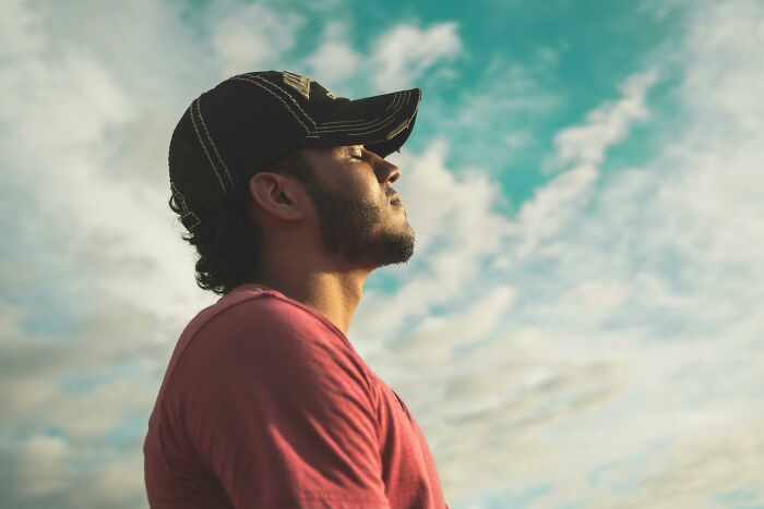 A person in a cap and t-shirt, standing outdoors, looking content, reflecting on the childfree lifestyle under a cloudy sky.