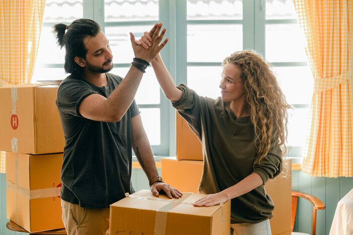 Two childfree individuals high-fiving near moving boxes in a bright room.