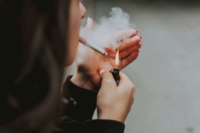 Person lighting a cigarette with a lighter, smoke rising; a prediction that aged badly.