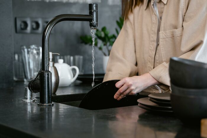 Person washing dishes in a kitchen, water flowing from the faucet, representing everyday mic-drop moments.