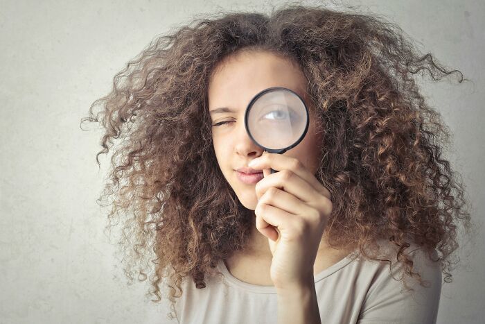 Woman holding a magnifying glass to her eye, illustrating attention to detail for a reality check quiz.