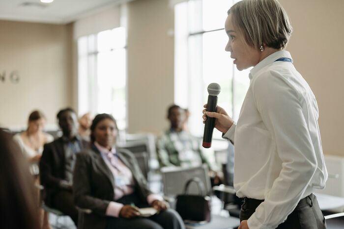 Person speaking into a microphone during a seminar, creating a potential mic-drop moment.