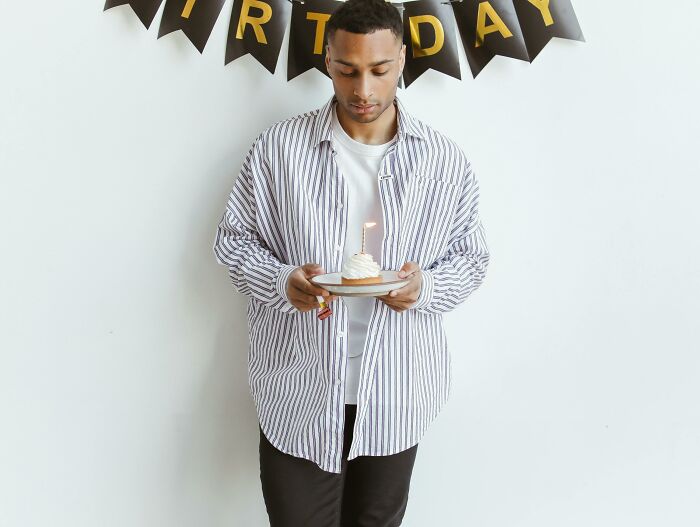 Person in a striped shirt holding a cupcake with a candle, standing under a "Birthday" banner, reflecting childfree life.