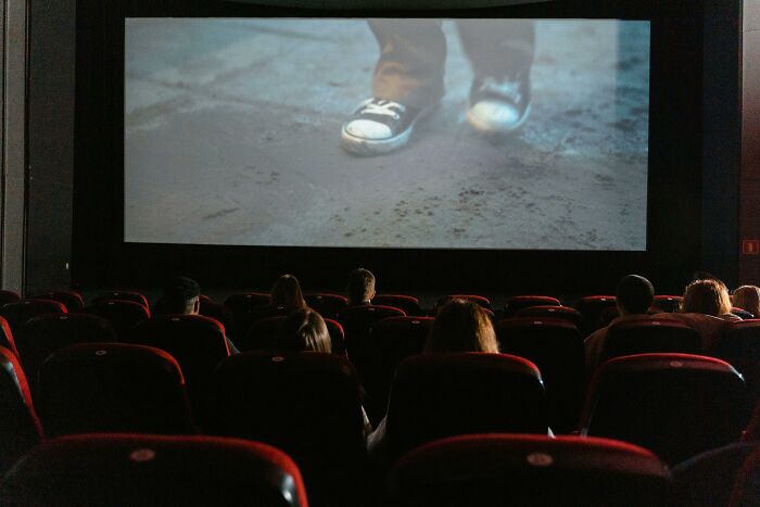 People watching a movie scene with shoes on a dirt floor in a cinema; prediction-themed film.