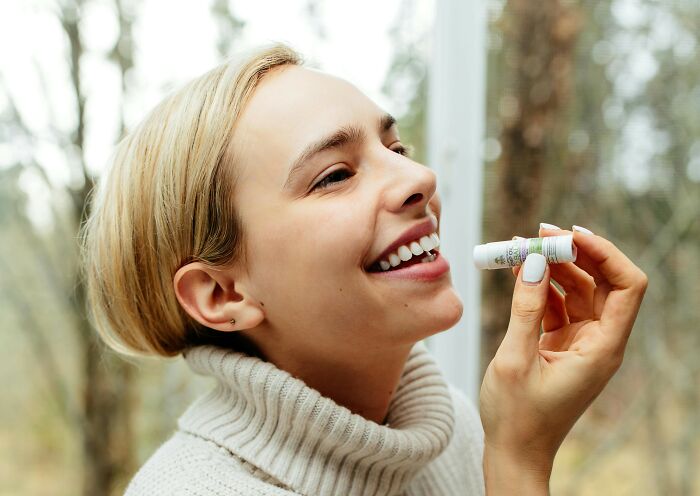 Woman smiling while applying lip balm, a travel must-have for packing efficiently.