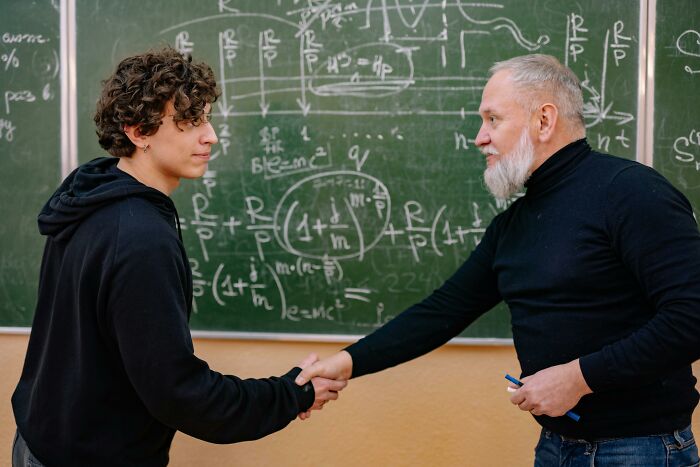 Student and teacher exchanging a handshake in front of a complex chalkboard, symbolizing mic-drop moments in learning.