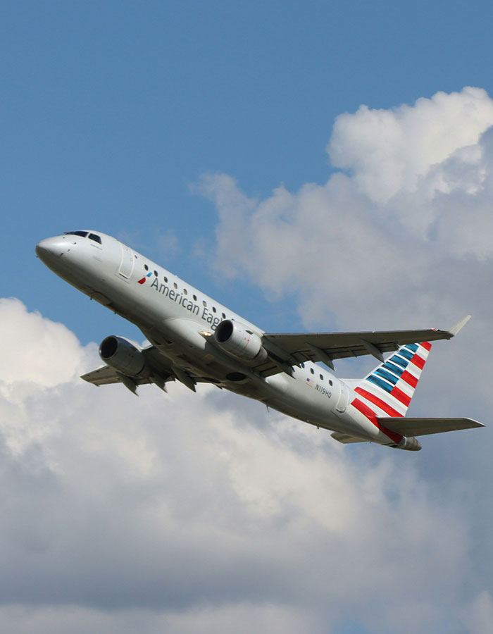 American Airlines plane flying under a blue sky with clouds.