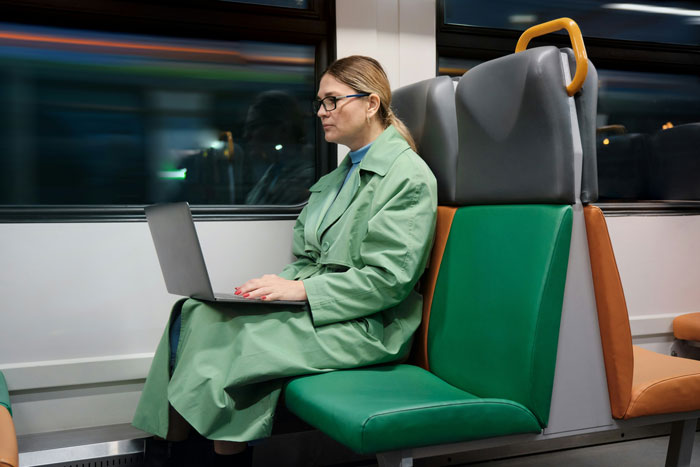 A woman in a green coat uses a laptop on a train seat, emphasizing the concept of prepaid train seat usage.