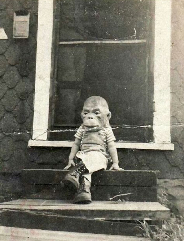 A child wearing a monkey mask and boots sitting on steps in a rare historical photo.