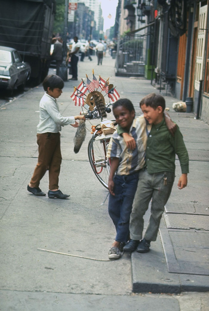 Children playing joyfully with a bicycle decorated with flags on a city street, capturing a rare historical moment.