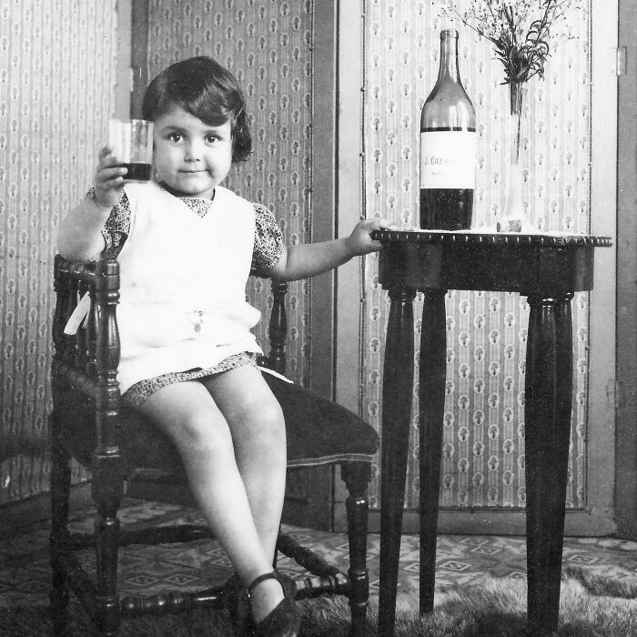 Young girl holding a glass next to a table with a bottle, representing rare historical photos.