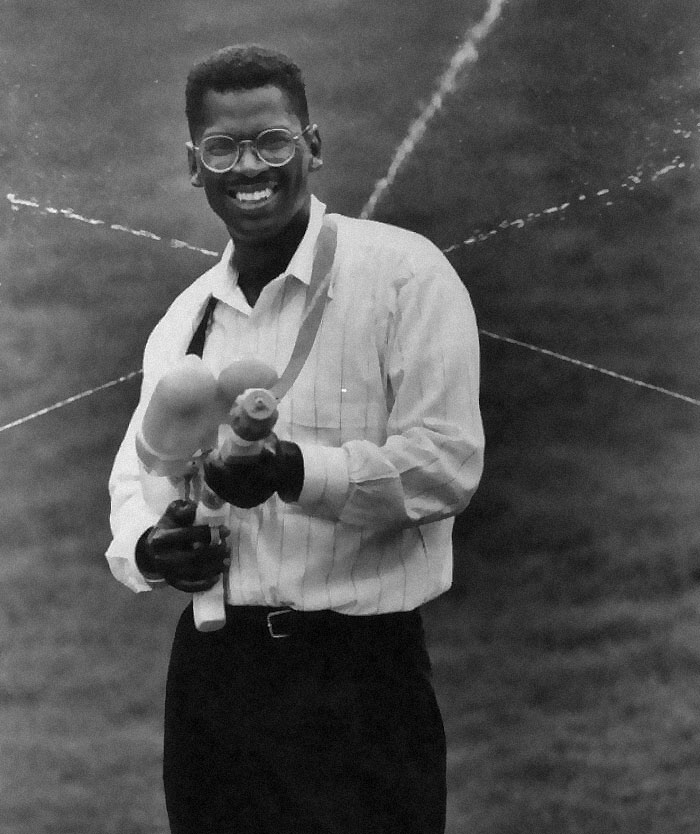 Smiling man in glasses holding a creative device, a rare historical photo capturing a joyful moment.