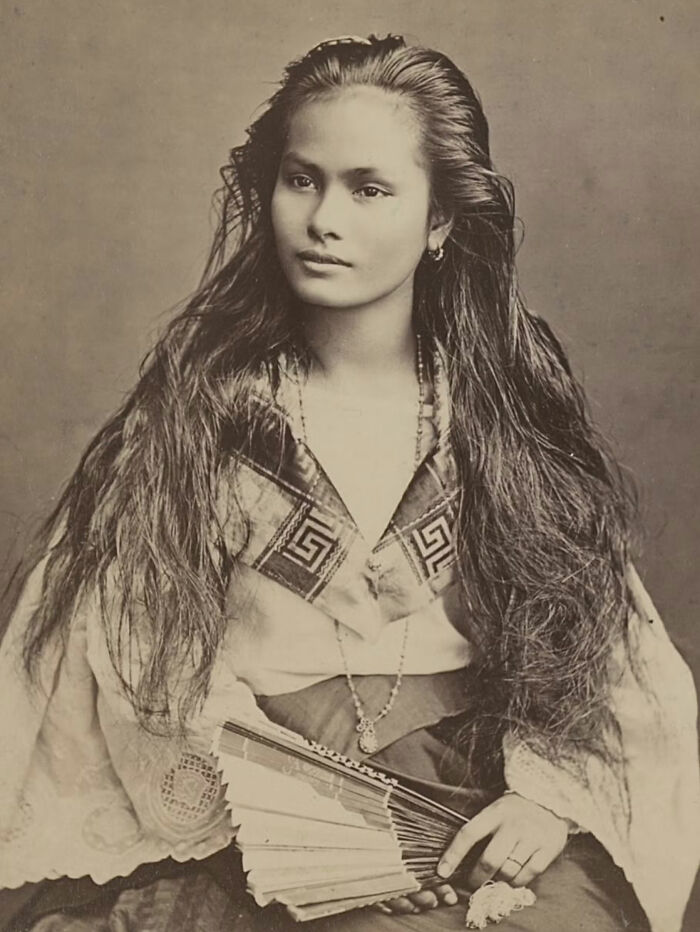 A rare historical photo of a woman with long hair, holding a fan, wearing traditional attire, offering a glimpse into the past.