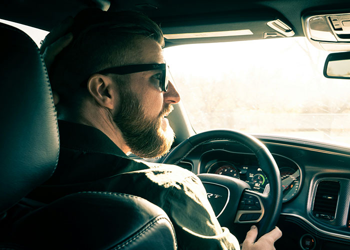 Man with sunglasses driving a car, focusing on the road, with sunlight streaming through the window.