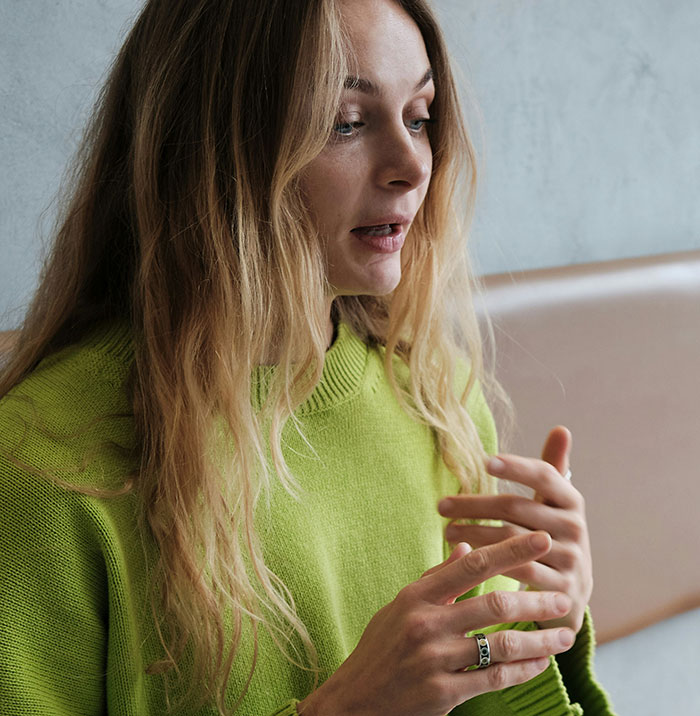 Woman in green sweater, gesturing while talking about family issues related to dad's ex-wife and son asking for help with rent.