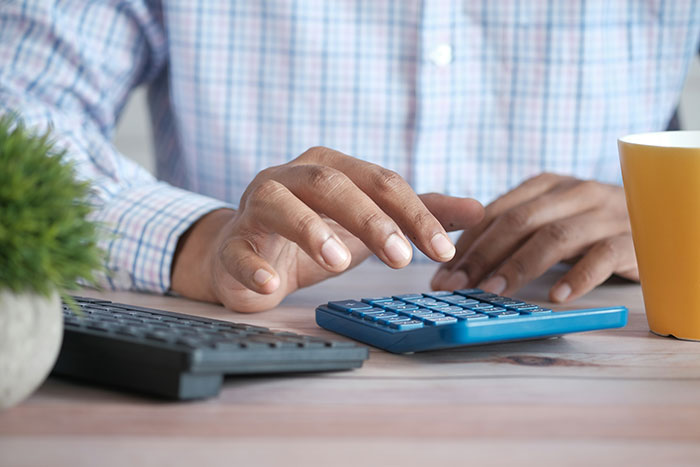 Hands using calculator on a desk with a cup, discussing rent payment issues.