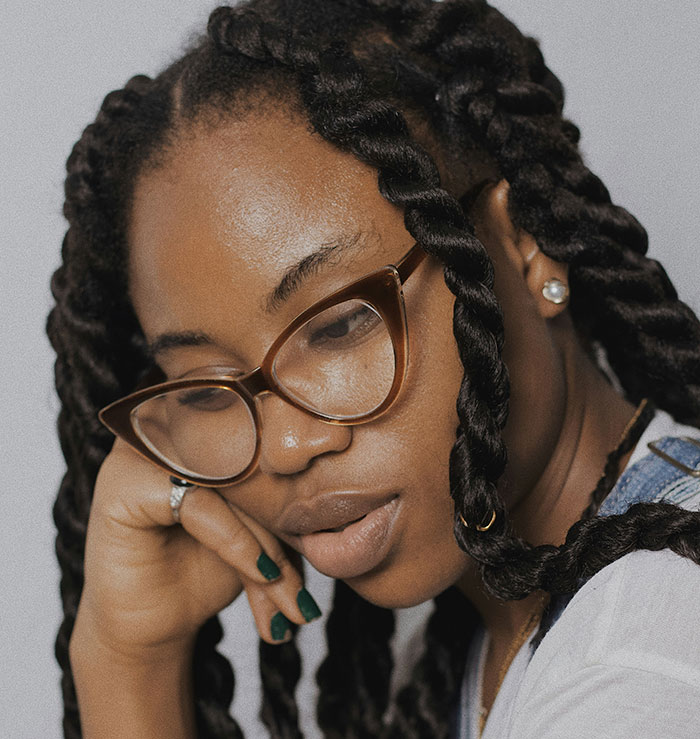 Young woman with glasses and braided hair, contemplating a decision about family and rent.