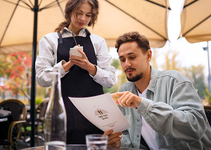 Man examining menu with waitress, illustrating restaurant manipulation tactics to encourage spending.